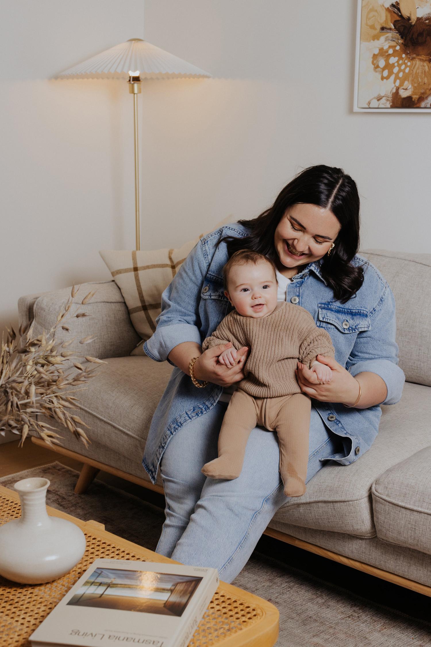 A joyful mother and baby bonding moment on a stylish beige sofa, surrounded by warm, minimalist home decor and natural elements for a serene, family-friendly vibe.