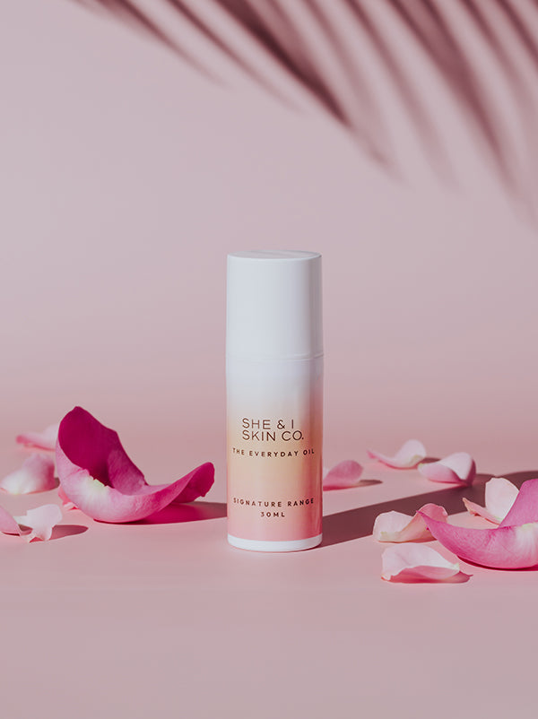  She & I Skin Co. "The Everyday Oil," 30ml, beautifully displayed with pink rose petals and soft palm shadows, evoking a sense of natural elegance and luxury skincare.