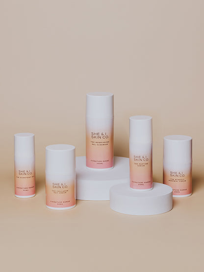 She & I Skin Co.'s skincare range, featuring cleansers, serums, and creams in gradient white-to-pink packaging.