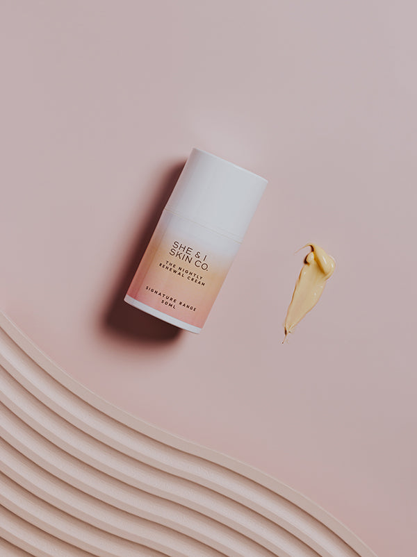 She & I Skin Co. "The Nightly Renewal Cream," 50ml, displayed with a golden cream smear on a soft pink background. Elegant textures evoke luxurious nighttime skincare rejuvenation.