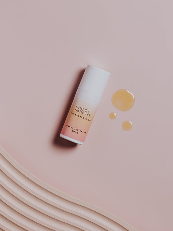 She & I Skin Co. "The Everyday Oil," showcased on a soft pink background with golden oil drops, highlighting its nourishing formula.